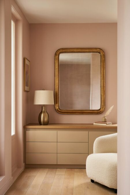 modern beige entryway chest of drawers, blush walls, a brass lamp, a gold gilded mirror, and a cream boucle barrel chair