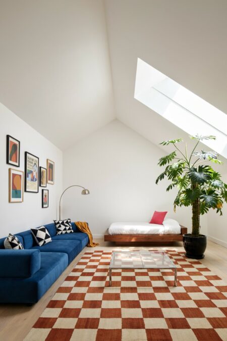 modern eclectic attic living room with a blue low sectional sofa, a platform daybed, a checkered rug, and a plant in a glossy black ceramic planter