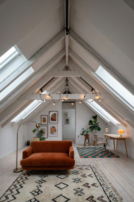modern eclectic attic living room with rugs in functional zones, a burnt orange velvet sofa, workspace with a small mushroom-shaped orange glass table lamp on the desk
