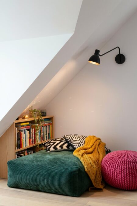 modern eclectic attic reading nook under the eaves, a narrow bookshelf, and a black wall sconce