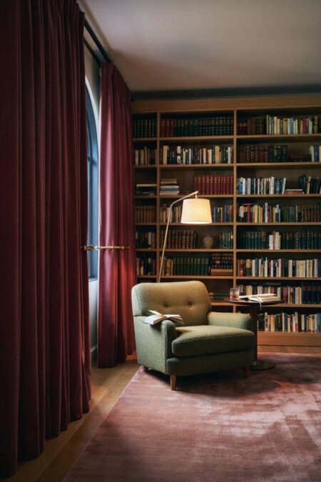 moody home library with burgundy velvet drapes, an olive accent chair, and a dusty pink rug
