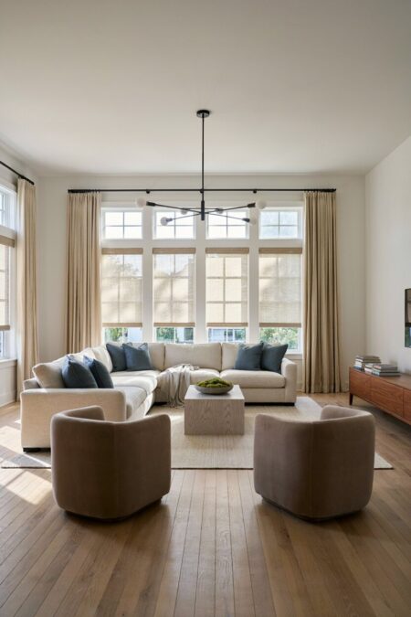 transitional living room with floor-length linen drapery panels, L-shaped sectional sofa with blue pillow, and barrel back accent chairs in taupe